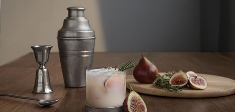 Cocktail shaker on table with jigger, fruit and a glass